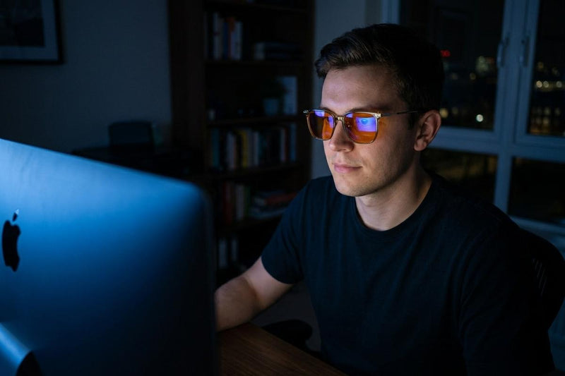 Man working at a computer late at night wearing amber-lens blue light glasses