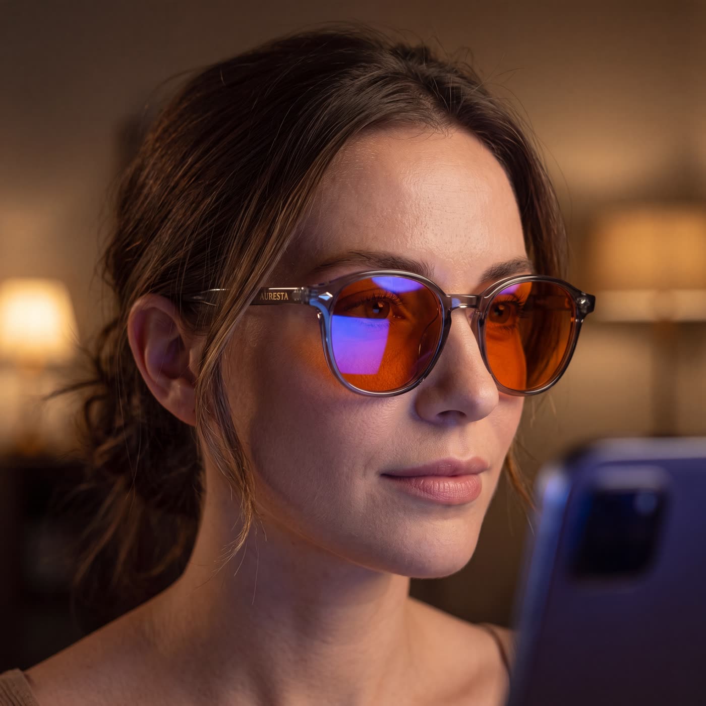 Scrolling a phone in bed at night wearing the Aura blue light glasses