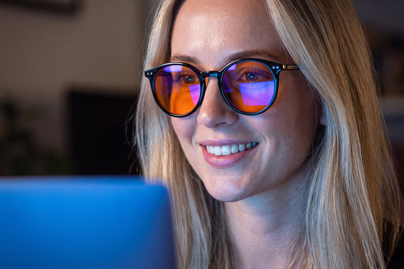 Auresta Raven blue light glasses — round black acetate with amber lenses, worn while working at a laptop