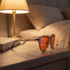 Aura blue light glasses on a bedside table beside a book and warm lamp