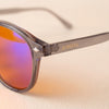 Close-up of the Aura blue light glasses — gold AURESTA lettering on the grey translucent TR90 temple and orange orange lens