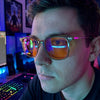 Close-up of a gamer wearing Olive blue light glasses at a neon-lit desk, orange lenses catching screen glow