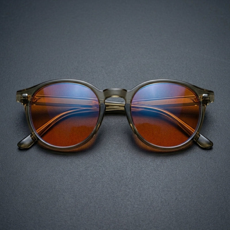 Folded Vesper blue light glasses shot head-on, showing round sage frame and warm orange lenses